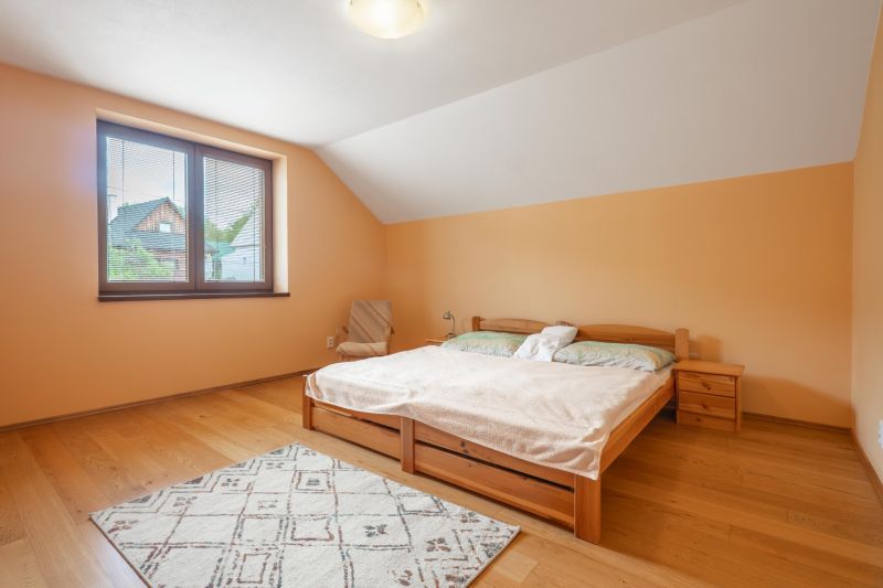 Ložnice s podlahou s dřevěným dekorem v rodinném domě, světlý nábytek a okno s výhledem.