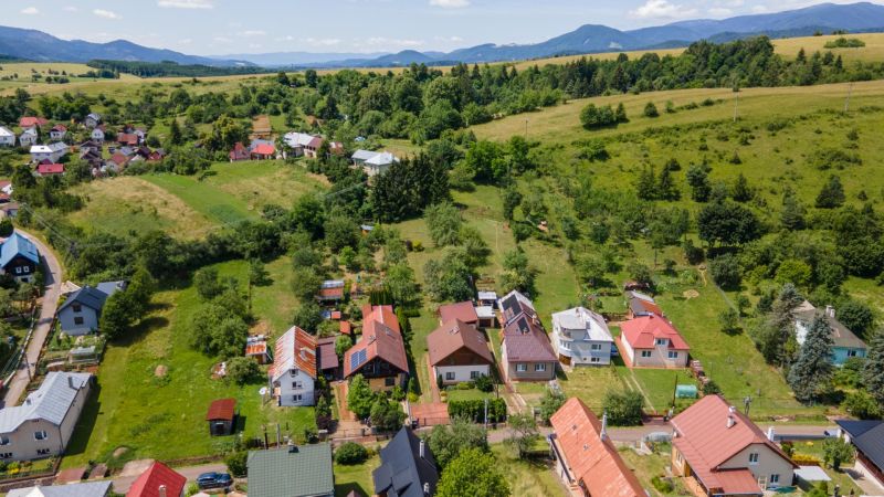 Pohled na rodinné domy v Horní Lhotě s kopcovitou krajinou v pozadí.
