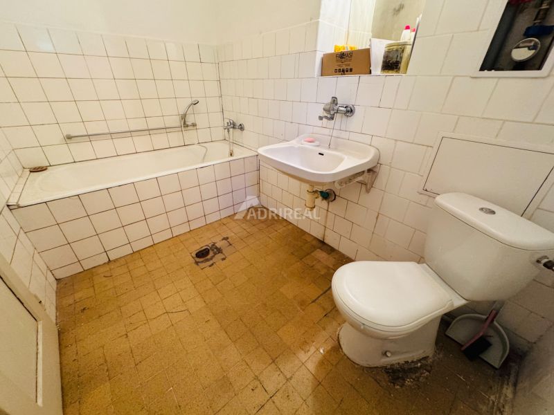 Koupelna v 2-pokojovém bytě s vanou, umyvadlem a toaletou, obložená bílými kachličkami.