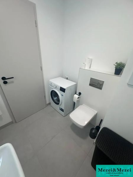 Koupelna s pračkou, toaletou a béžovou dlažbou v 2-pokojovém bytě.