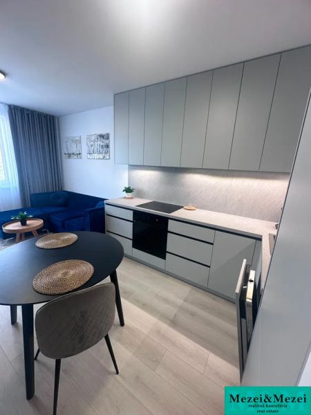 Kuchyňský kout s varnou deskou, kulatý stůl, sedačka, podlaha s dřevěným dekorem.