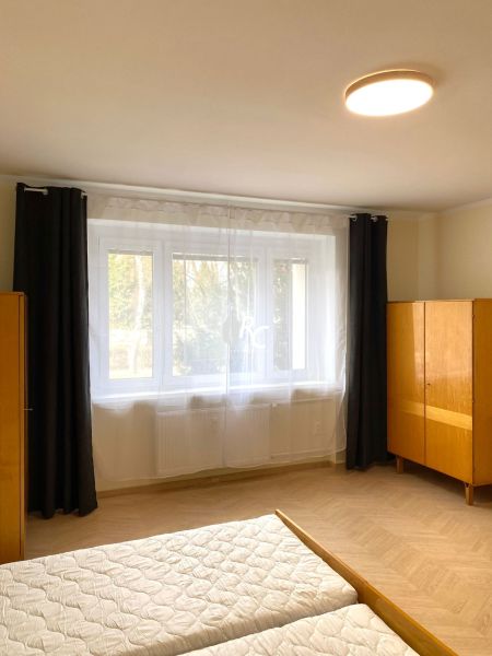 Světlá ložnice s velkým oknem a podlahou s dřevěným dekorem ve 3-pokojovém bytě.