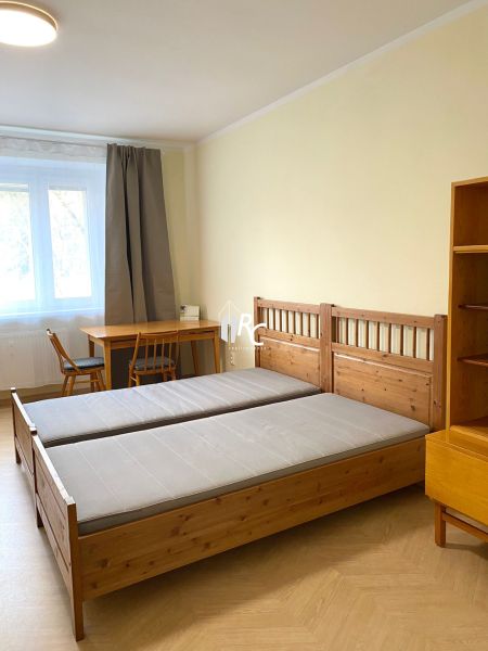 Ložnice s dřevěnými postelemi, stolem a podlahou s dřevěným dekorem v třípokojovém bytě.