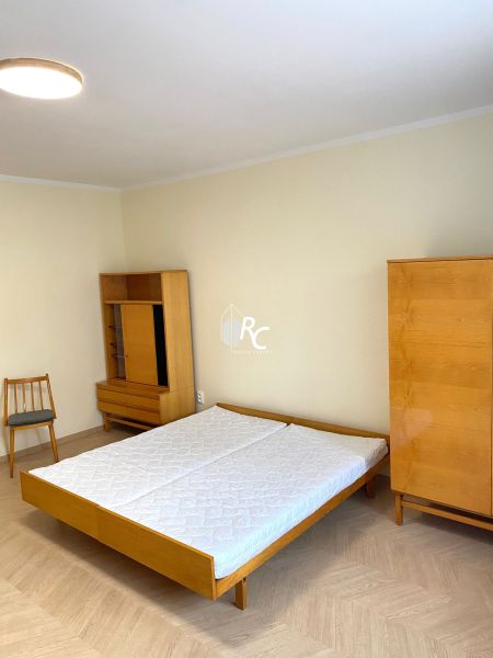 Ložnice s postelí, skříní a podlahou s dřevěným dekorem ve 3-pokojovém bytě.