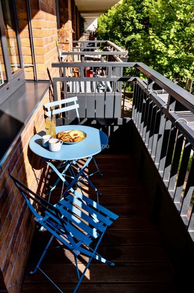 Balkon 2-pokojového bytu s modrým stolem a židlemi, dřevěná podlaha, pevné zábradlí.