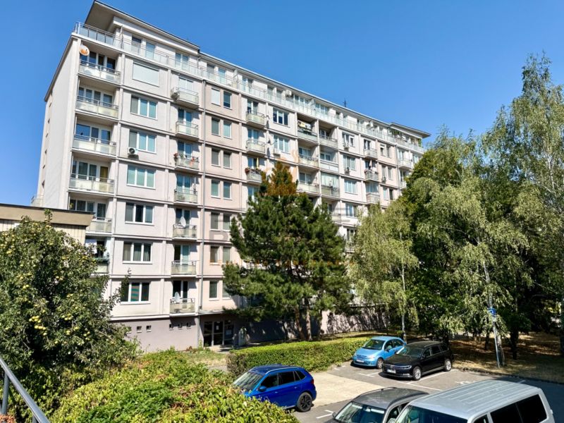 Bytový dům na Piešťanské ulici v Bratislavě - Nové Město obklopený zelení a parkovištěm.