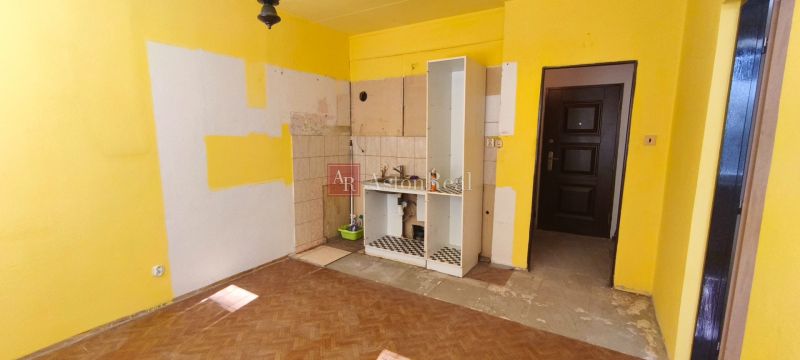 Žluté stěny s rozpracovanou kuchyní a podlahou s dřevěným dekorem v 1-pokojovém bytě.