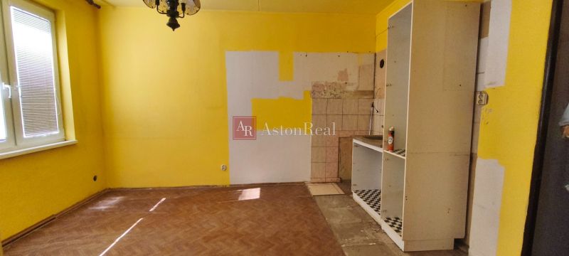 Žluté stěny, nedokončená kuchyň, podlaha s dřevěným dekorem v 1-pokojovém bytě.