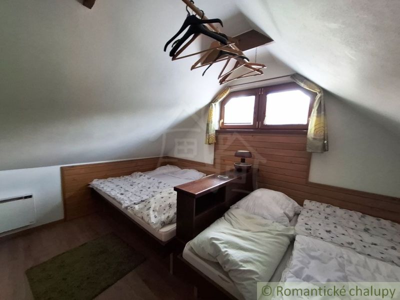 Podkroví se dvěma postelemi, podlaha s dřevěným dekorem, věšáky, malé okno, nízký strop.