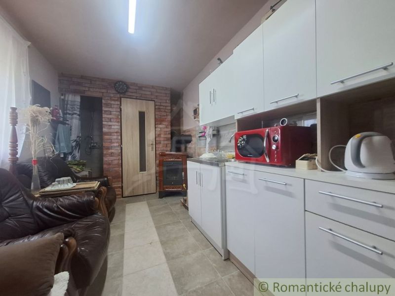 Kuchyně v chatě s bílými skříněmi, červenou mikrovlnkou a koženými pohovkami.