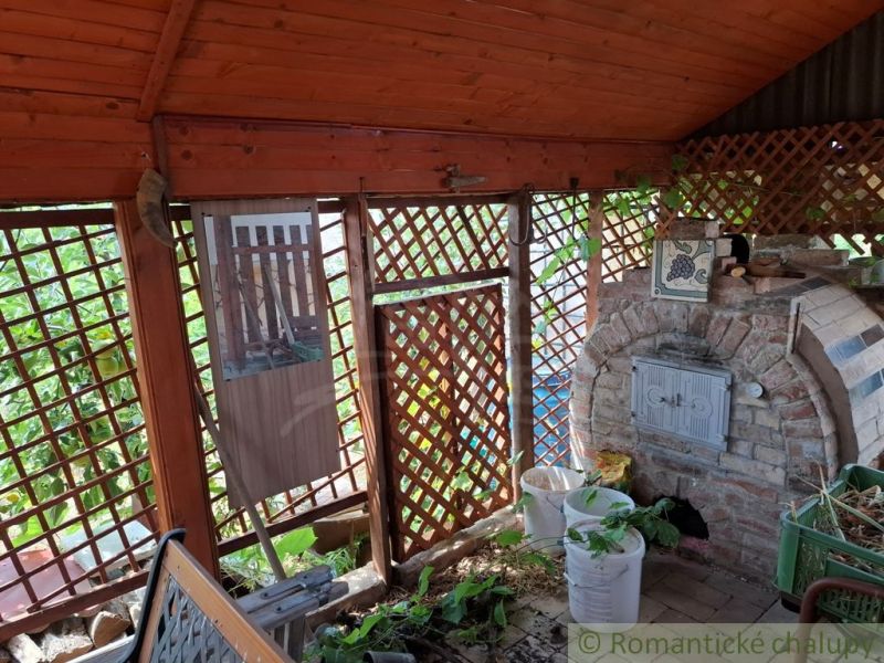 Krytá terasa chaty v Gbelcích s cihlovým venkovním krbem a rostlinami.