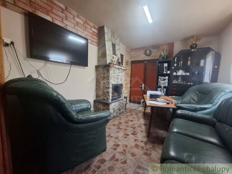 Kamenný krb a kožené sedačky v chatě s podlahou ve stylu dlaždic.