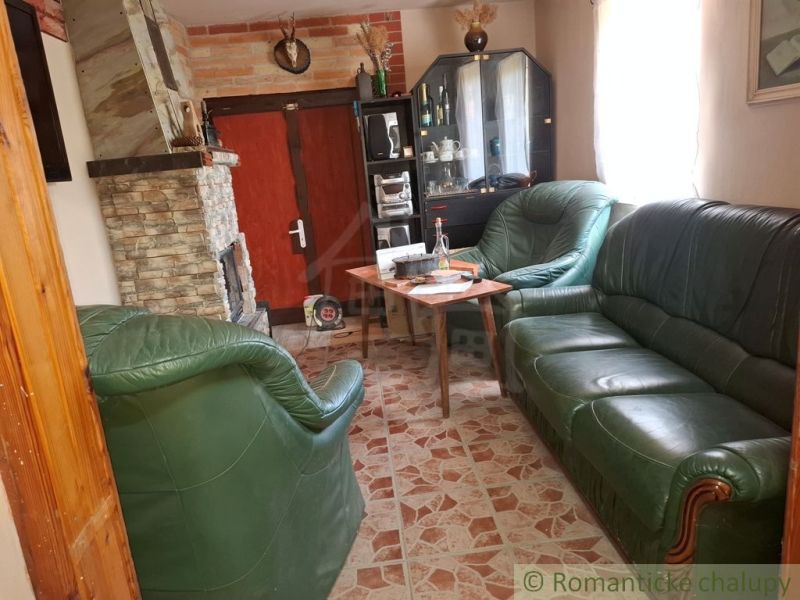 Interiér chaty s krbem, koženou sedací soupravou a vitrínou na podlaze s dřevěným dekorem.