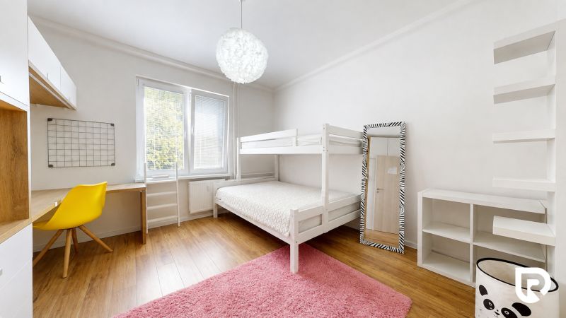 Dětský pokoj ve 3-pokojovém bytě s palandou, žlutou židlí, regály a podlahou s dřevěným dekorem.