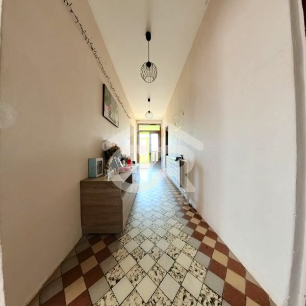 Chodba rodinného domu s dlaždicovou podlahou, komodou a lampami na stropě.