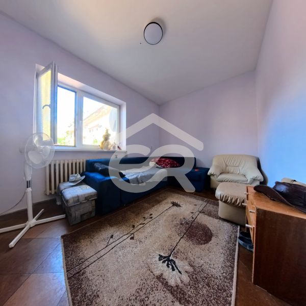 Obývací pokoj v rodinném domě s modrou pohovkou, křeslem a kobercem na podlaze s dřevěným dekorem.