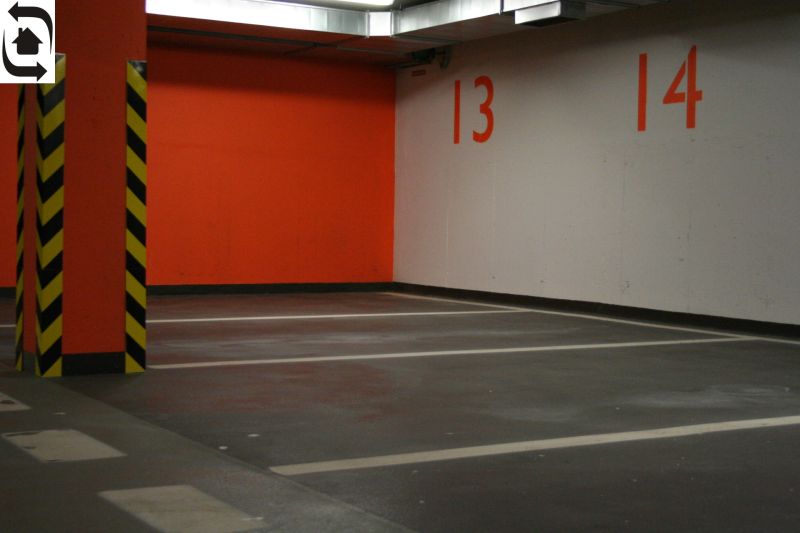 Parkovací místa a oranžová zeď v garáži se žlutými a černými sloupy.