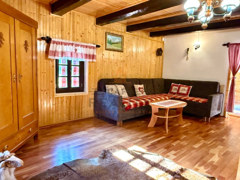 Interiér rodinného domu s rohovou sedačkou, skříňkou a podlahou s dřevěným dekorem.