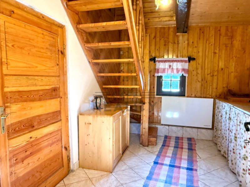 Interiér rodinného domu s dřevěným schodištěm, stropem a dveřmi, dlažba na podlaze.