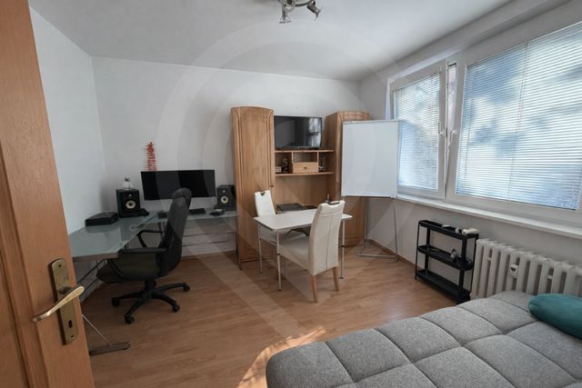 Interiér 3-pokojového bytu s podlahou s dřevěným dekorem, pracovním stolem a pohovkou.