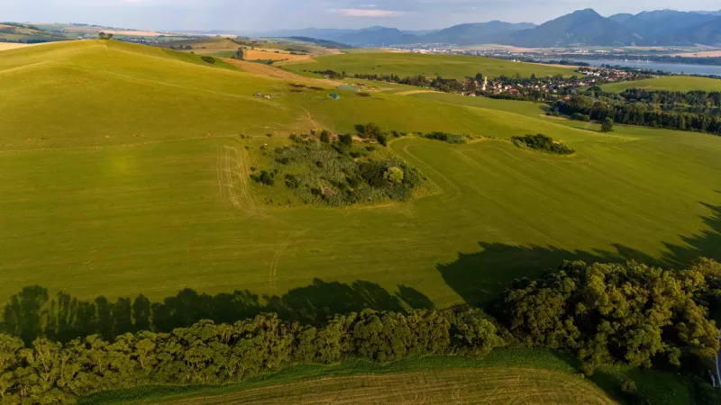 Rozsáhlé zelené pole a kopce v Liptovském Trnovci, nabízející pohled na zvláštní nemovitosti.