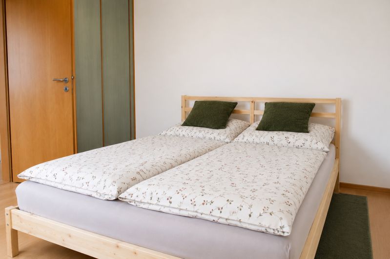 Ložnice s manželskou postelí, polštáři v 2-pokojovém bytě na podlaze s dřevěným dekorem.