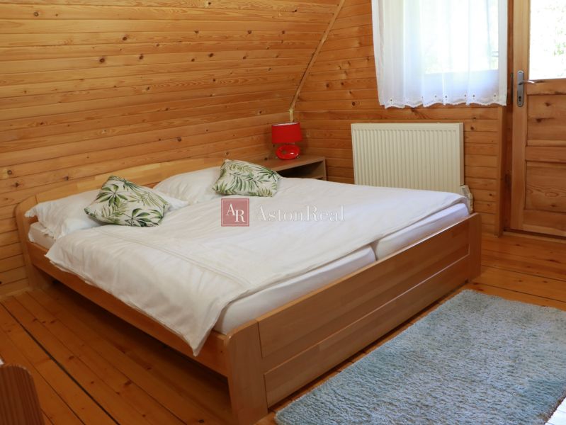 Ložnice v chatě s dřevěným obkladem, postelí a podlahou s dřevěným dekorem.