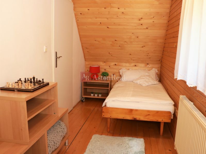 Jednolůžkový pokoj s podlahou s dřevěným dekorem, šachovnicí na stolku a oknem s bílou záclonou.