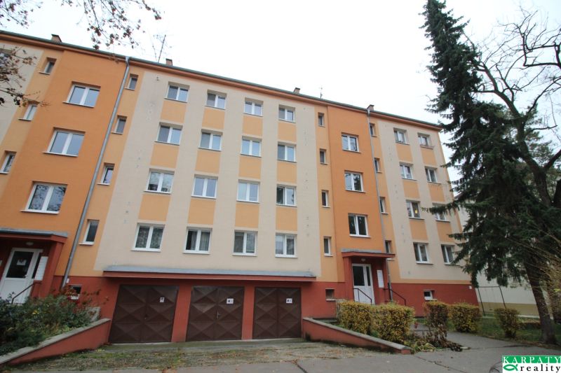 Bytový dům v Trnavě s barevnou fasádou, garážemi a okolím se stromy.