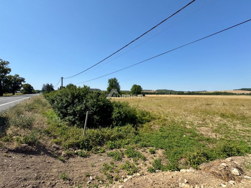 Pozemky na bydlení v Hokovcích, vedle cesty, s elektrickými vedeními nad nimi.