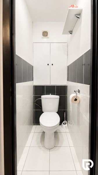 Toaleta s bílými a šedými dlaždicemi, úložný prostor nad WC.