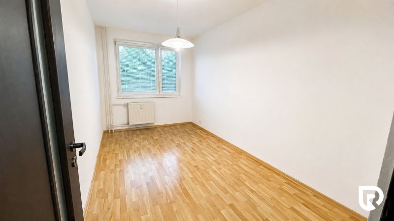 Prázdný pokoj v dvoupokojovém bytě s podlahou s dřevěným dekorem a bílými stěnami.