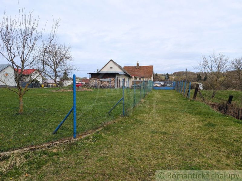 Rodinný dům v obci Volica s trávníkem a modrým plotem, bez listí na stromech.