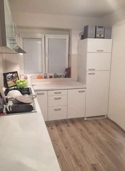 Kuchyně v 2-pokojovém bytě s bílými skříňkami a podlahou s dřevěným dekorem.