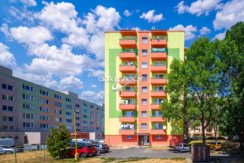Barevné bytové domy na Sládkovičově ulici ve Fiľakovu s parkovištěm a zelení.