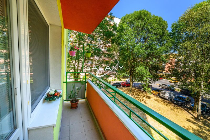 Balkon 2-pokojového bytu na Sládkovičově ulici ve Fiľakovu, lemovaný zelení, s květinami.