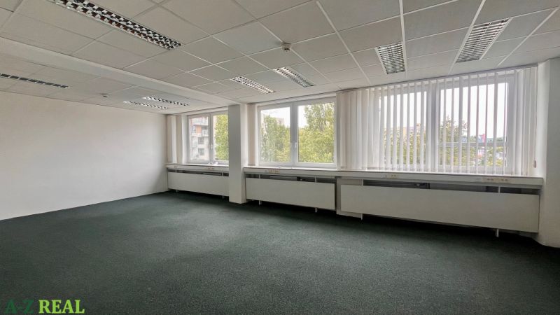 Prázdné kanceláře s velkými okny a kobercovou podlahou.