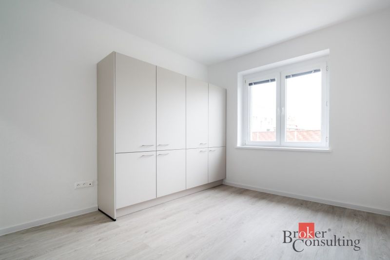 Světlý pokoj s bílou skříní a podlahou s dřevěným dekorem ve 3-pokojovém bytě.