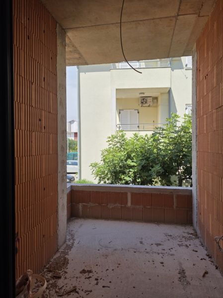 Nedokončený balkon v 3-pokojovém bytě s výhledem na zeleň a sousední budovu.