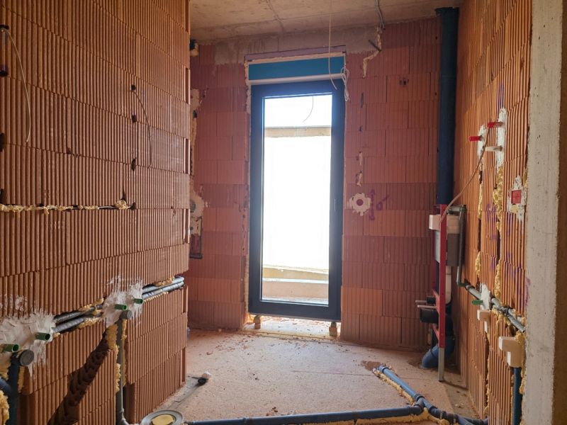 Nedokončená místnost se surovými cihlovými stěnami a východem na balkon v 3-pokojovém bytě.