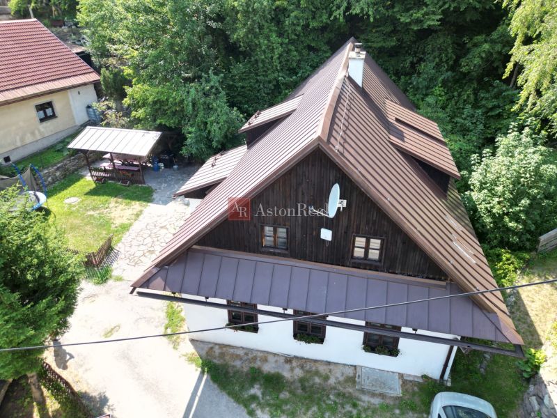 Rodinný dům ve Španí Dolině s dřevěným obkladem a okolím plným zeleně.