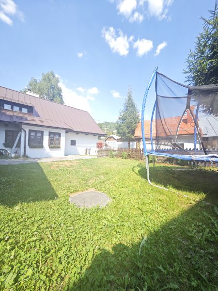 Chata ve Španělé Dolině s trampolínou na travnaté zahradě pod modrou oblohou.