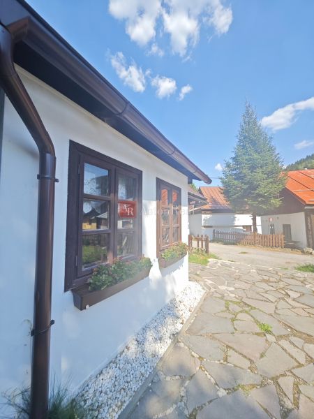 Chata ve Španí Dolině se záhonem u okna a dlážděným chodníkem.