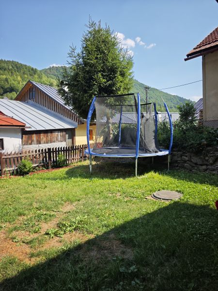 Trampolína u chaty ve Španej Dolině, obklopená trávou a stromy v pozadí.