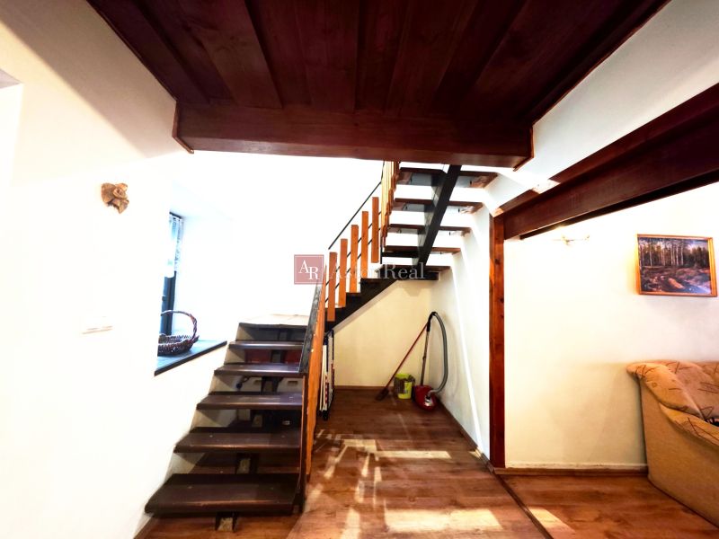 Interiér chaty s dřevěným schodištěm a podlahou s dřevěným dekorem.