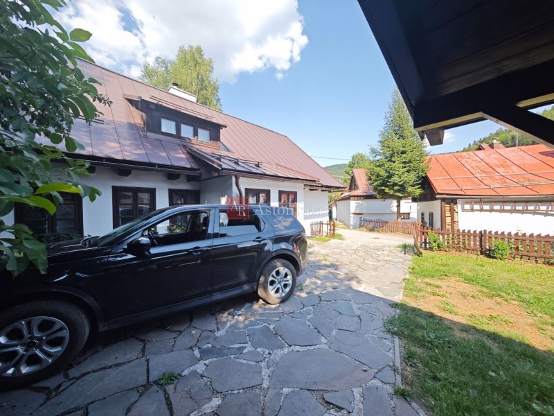 Auto zaparkované u chaty ve Španí Dolině, s viditelnými střechami a plotem.