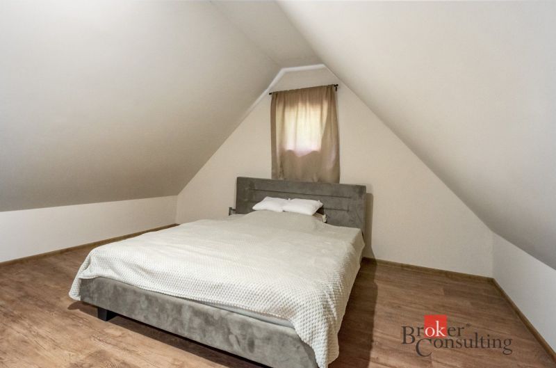 Podkrovní ložnice na chatě s postelí a podlahou s dřevěným dekorem.