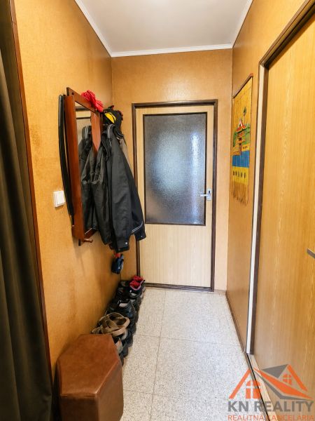 Chodba v rodinném domě s věšákem na šaty a botníkem, neutrální odstíny.