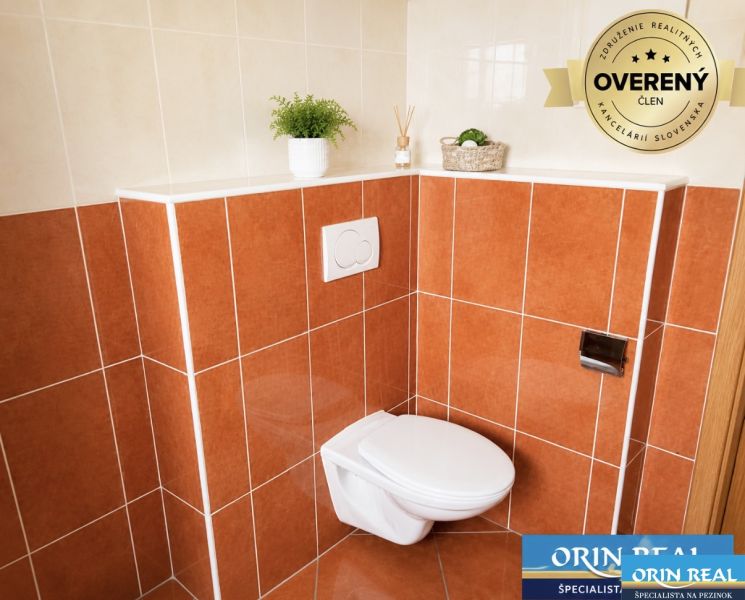 Koupelna s oranžovými obklady a závěsným WC v 1-pokojovém bytě.