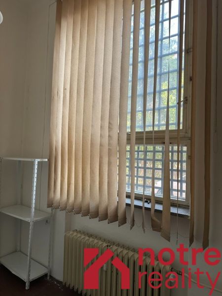 Kanceláře s vertikálními žaluziemi a policovým regálem, podlaha s dřevěným dekorem.